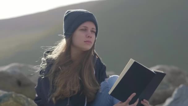 Meisje zit aan de kust en leest een boek — Stockvideo