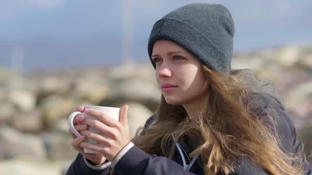 Fille s'assoit sur les rochers tout en buvant une tasse de café — Video