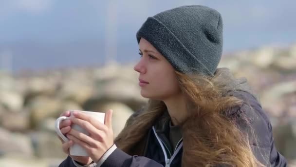 Mooi meisje zit aan de oceaan met een kopje koffie — Stockvideo