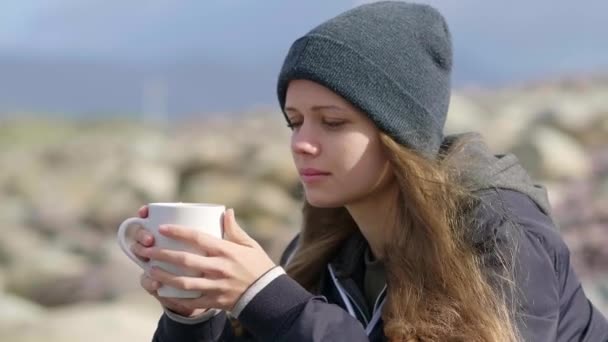 Menina bonita senta-se sozinho no oceano e bebe uma xícara de café — Vídeo de Stock