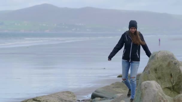 Красивая девушка перелезает через большие скалы на набережной — стоковое видео