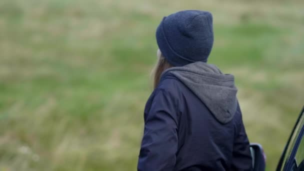 Ragazza si trova accanto alla sua auto e guarda oltre la natura verde — Video Stock