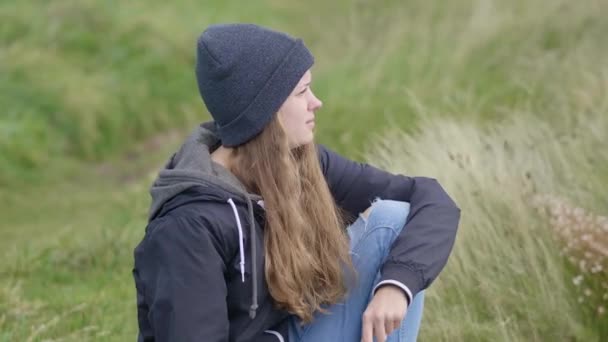 Mujer joven se sienta en la hierba profunda y disfruta del paisaje — Vídeos de Stock