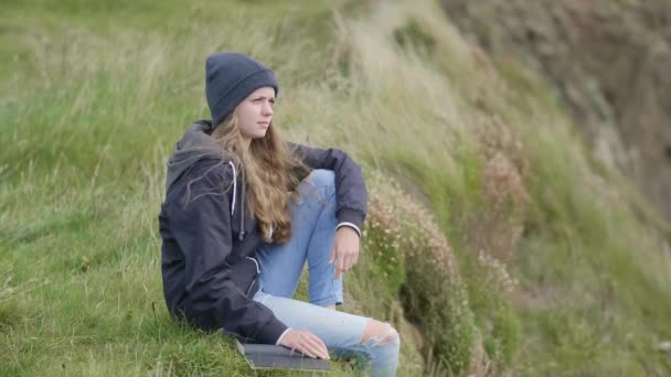 Mujer joven se sienta en la hierba en el borde de un acantilado — Vídeos de Stock