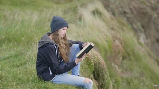 Όμορφο κορίτσι διαβάζει ένα βιβλίο ενώ χαλαρώνετε στους τομείς γρασίδι — Αρχείο Βίντεο
