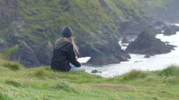 Молода жінка читає книгу, відпочиваючи на набережній — стокове відео