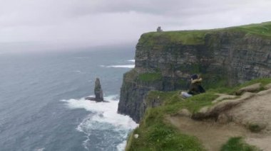 Genç kadın, tek başına Moher kayalıklarla oturur