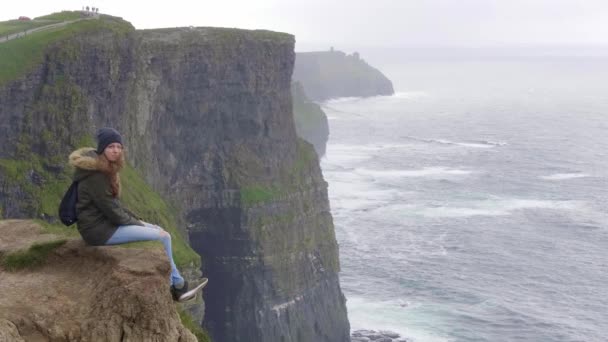 Fantastisk utsikt över en flicka sitter på kanten av Cliffs of Moher — Stockvideo