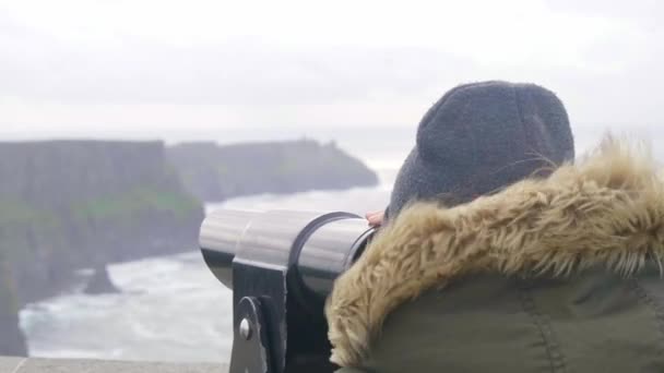 Meisje kijkt door een spyglass over de Cliffs of Moher in Ierland — Stockvideo