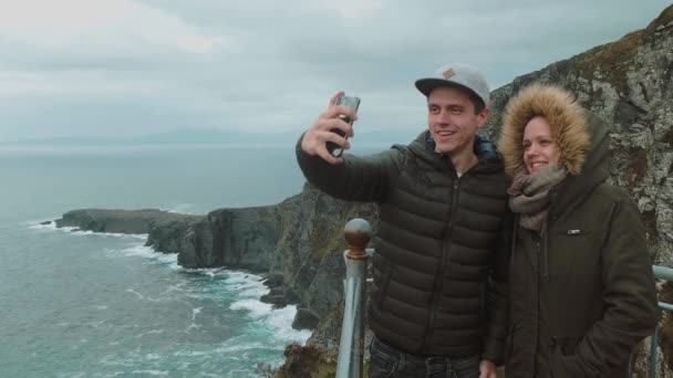 Casal jovem fica nos penhascos íngremes da Irlanda e tirar uma selfie — Vídeo de Stock