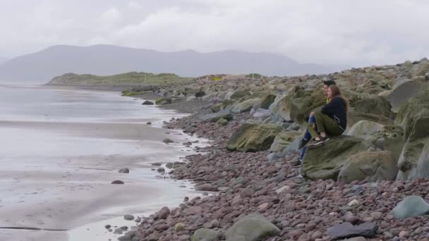 Casal jovem senta-se em uma rocha na costa oeste irlandesa — Vídeo de Stock