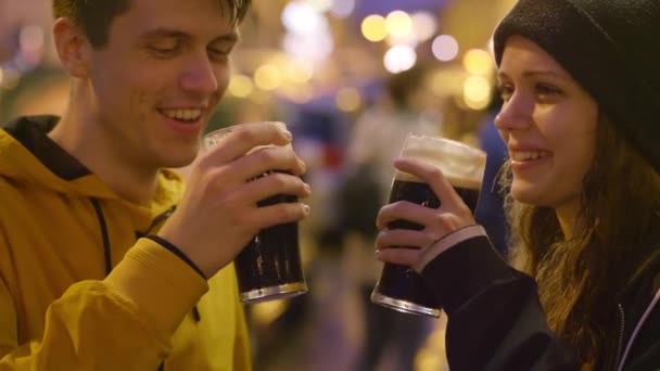 Twee vrienden zeggen cheers en drinken bier vóór een pub — Stockvideo