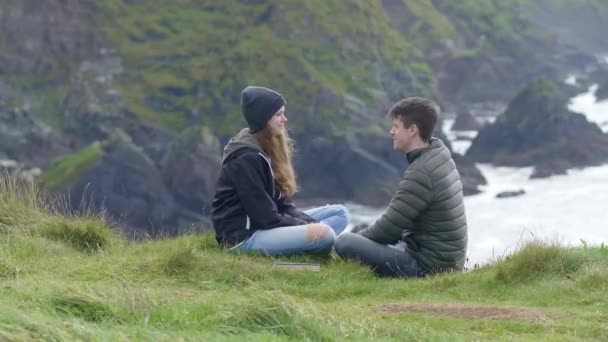 Dos amigos se sientan en la hierba en la cima de los acantilados — Vídeos de Stock
