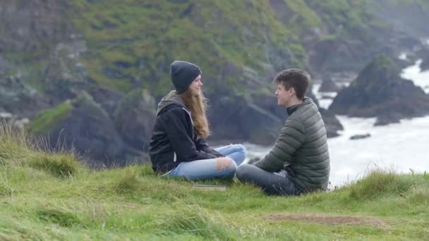 Twee vrienden zitten in het gras op de top van de kliffen — Stockvideo