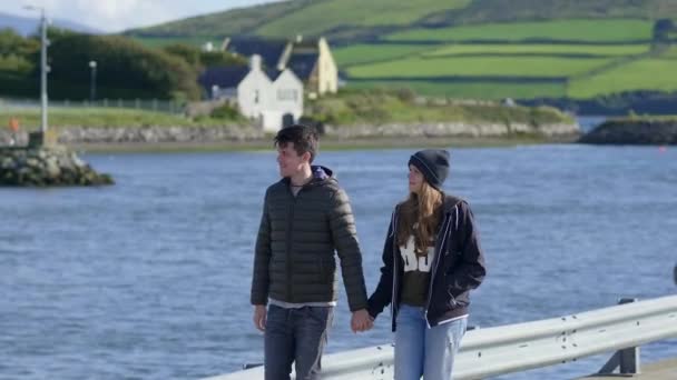 Молодая пара идет рука об руку через гавань — стоковое видео