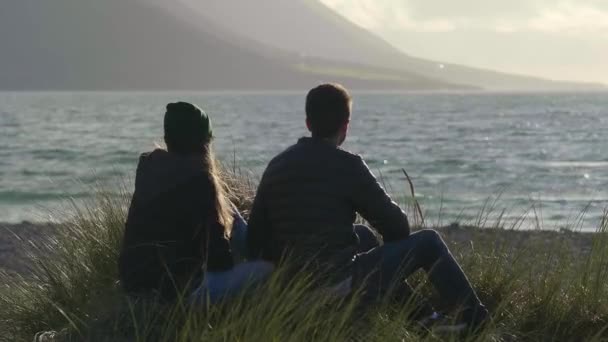 Para siedzi Oceanfront oglądając zachód słońca — Wideo stockowe