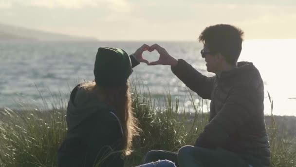 Dos amigos forman la forma de un corazón sentado en la playa — Vídeos de Stock