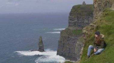 Moher Cliffs at çim güzel kız oturuyor
