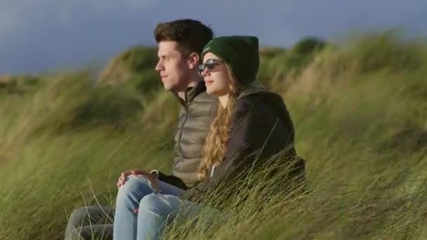 Två vänner sitta i reed gräs och vaka över solnedgången — Stockvideo