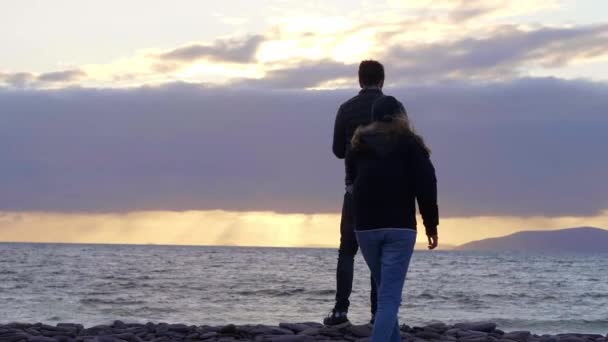 Pareja joven enamorada disfruta de la puesta de sol sobre el océano — Vídeo de stock