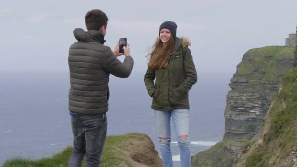 Giovane uomo prende una foto della sua ragazza alle scogliere di Moher — Video Stock