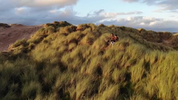 Pareja joven disfruta de la puesta de sol mientras se sienta en una colina cubierta de hierba — Vídeos de Stock