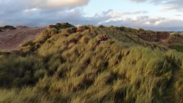 Flucht in Richtung eines jungen Paares, das auf den grasbewachsenen Hügeln an der Küste sitzt — Stockvideo