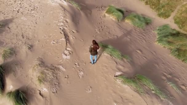 Aerial view over a girl standing on the top of sand dunes at the coast — Stock Video