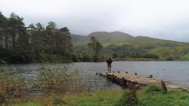 Jovem mulher fica em um cais em um belo lago na Irlanda — Vídeo de Stock