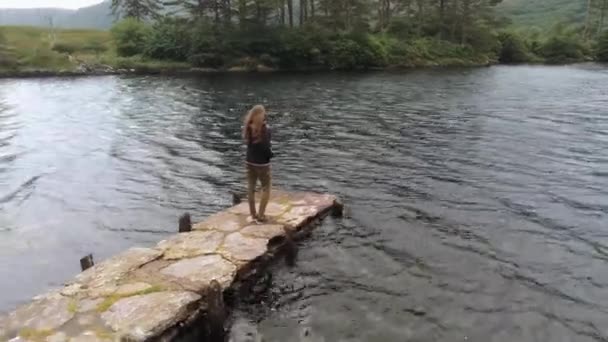 Jonge vrouw staat op een pier bij een prachtig meer in Ierland — Stockvideo