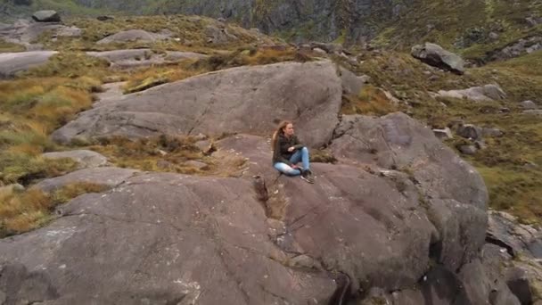 Полет назад от девушки, сидящей на камне — стоковое видео