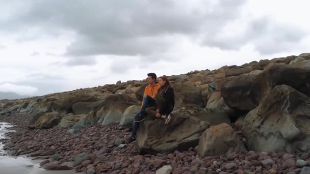 Två vänner sitta på en klippa och ser ut över havet — Stockvideo