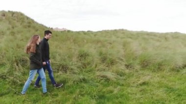 Genç bir çift bir çim alan İrlandalı sahilinde size yürür