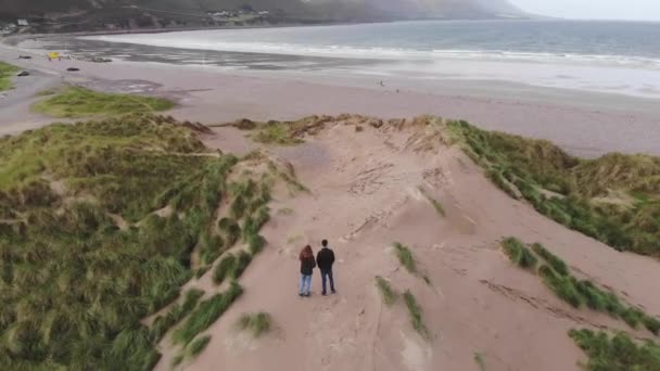 Pareja joven disfrutando de la vista sobre el océano desde las dunas — Vídeos de Stock