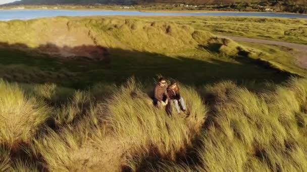 アイルランドの西海岸で砂丘に座っているカップルの周りの飛行 — ストック動画