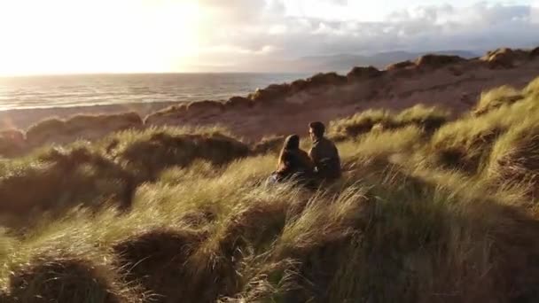 Молодая влюбленная пара наслаждается закатом над океаном — стоковое видео
