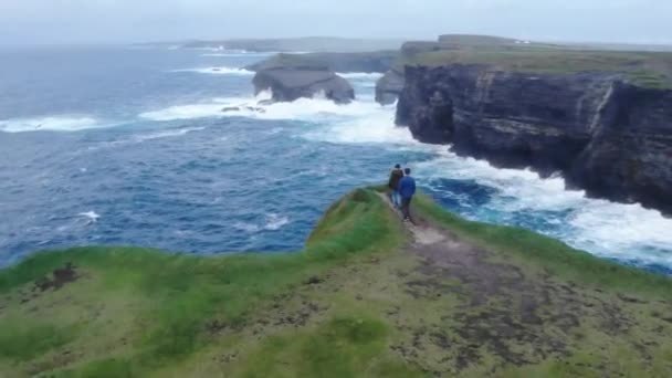 Fiatal pár sétál a szélén egy sziklán ír nyugati partvidékén — Stock videók