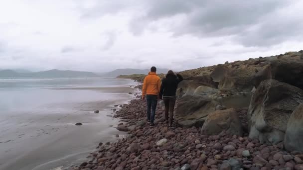 Két barátok séta a kavicsos strand ír nyugati partvidékén — Stock videók
