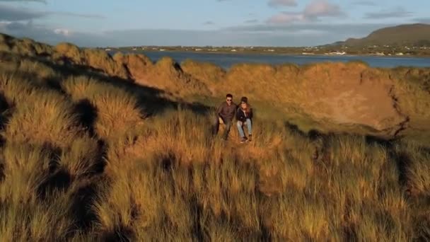 Et ungt par sitter i gresset og nyter solnedgangen – stockvideo