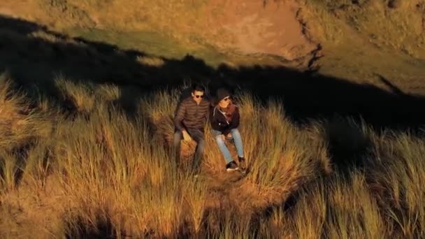 Paar zit op een met gras begroeide heuvel en kijken naar de zonsondergang — Stockvideo