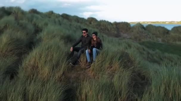 Vuelo alrededor de una joven pareja que se sienta en la cima de una colina en la costa — Vídeo de stock
