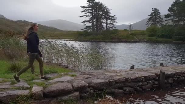 Wanita muda berjalan di atas dermaga menuju sebuah danau yang indah di Irlandia — Stok Video