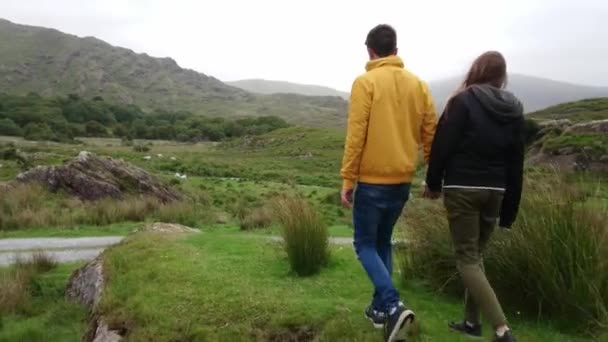 Junges Paar wandert Hand in Hand durch die typische Landschaft Irlands — Stockvideo