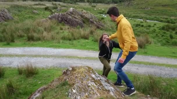 Young man helps his girlfriend to climb up a rock — Stock Video