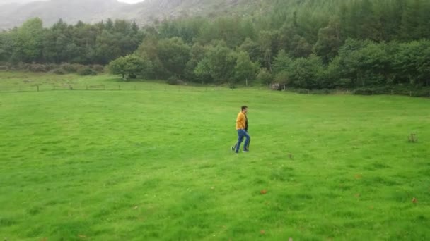 Jovem casal caminhar sobre um pasto verde em um dia chuvoso — Vídeo de Stock
