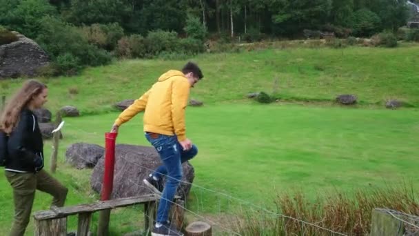 Jeune homme aide sa petite amie à grimper sur une clôture — Video