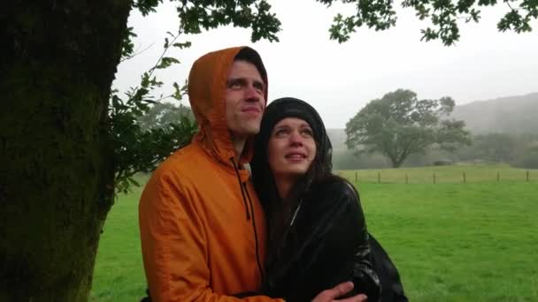 Mladý pár tváří v tvář silné deště hledá přístřeší pod stromem — Stock video