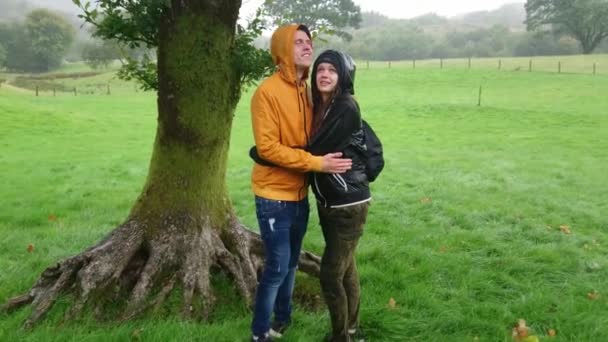 Молодая влюбленная пара ждет под деревом, пока дождь не прекратится — стоковое видео