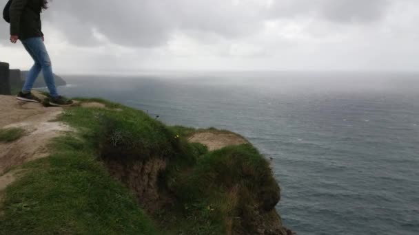 Odvážná dívka sedí na okraji strmé útesy Moher v Irsku — Stock video