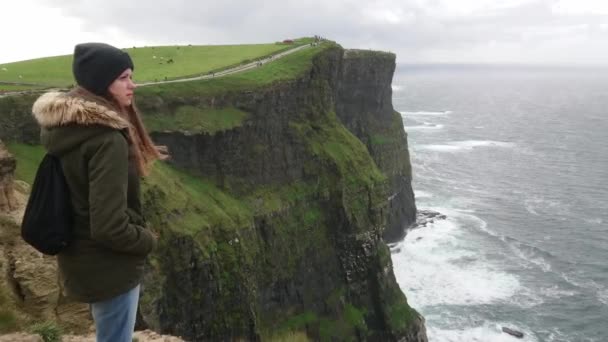 Söt flicka står vid kanten av branta Cliffs of Moher på Irland — Stockvideo